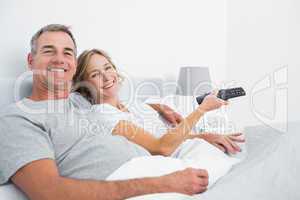 Happy couple cuddling in bed watching television