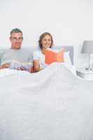 Smiling couple sitting in bed reading books