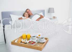 Loving couple sleeping with breakfast tray on bed