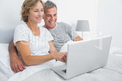 Smiling couple using their laptop together in bed