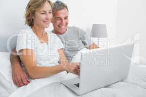 Smiling couple using their laptop together in bed