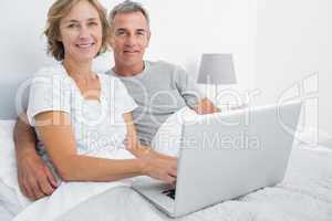 Relaxed couple using their laptop together in bed