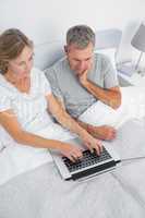 Thoughtful couple using their laptop together in bed