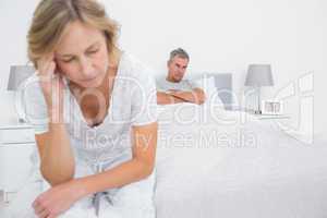 Unhappy couple sitting on opposite ends of bed after a fight