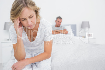 Upset couple sitting on opposite ends of bed after a fight