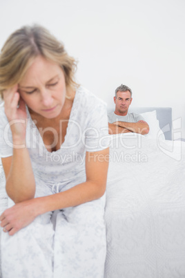 Annoyed couple sitting on opposite ends of bed after a fight