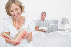 Woman reading book while husband is using laptop