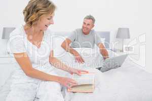 Smiling woman reading book while husband is using laptop