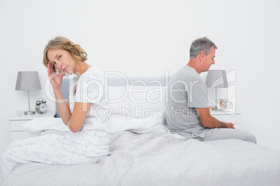 Annoyed couple sitting on different sides of bed having a disput
