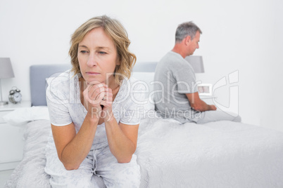 Unhappy couple sitting on different sides of bed having a disput
