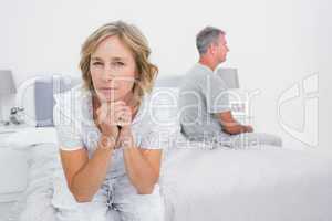 Thoughtful couple sitting on different sides of bed having a dis