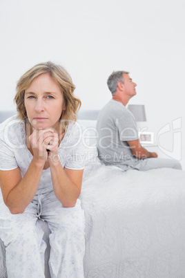 Fed up couple sitting on different sides of bed having a dispute