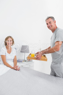 Smiling husband bringing breakfast in bed to wife