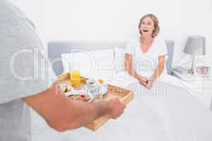 Husband bringing breakfast in bed to surprised wife