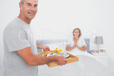 Happy husband bringing breakfast in bed to delighted wife