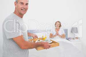 Happy husband bringing breakfast in bed to delighted wife
