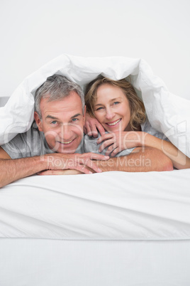 Cheerful middle aged couple under the duvet