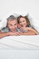 Cheerful middle aged couple under the duvet