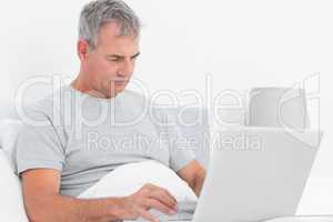 Grey haired man using his laptop in bed