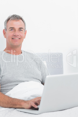 Smiling grey haired man using his laptop in bed