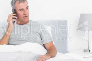 Grey haired man making a phone call in bed