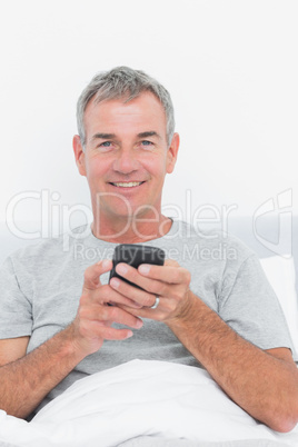 Happy grey haired man sending a text in bed