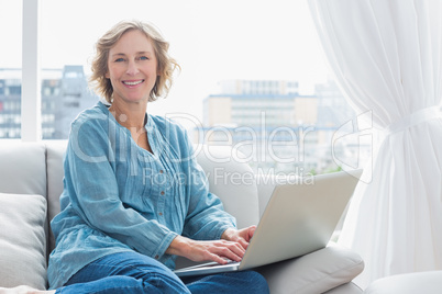 Content blonde woman sitting on her couch using laptop
