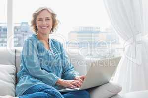 Content blonde woman sitting on her couch using laptop