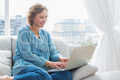 Happy blonde woman sitting on her couch using laptop Happy blonde woman sitting on her couch using laptop