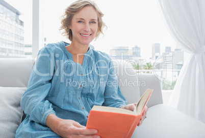 Content blonde woman sitting on her couch holding a book