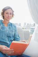 Content blonde woman sitting on her couch reading a book