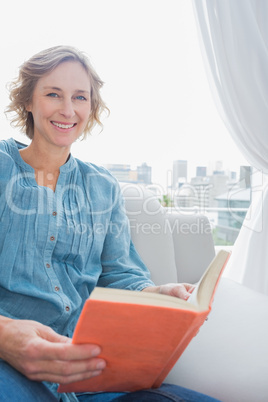 Blonde woman sitting on her couch reading a book