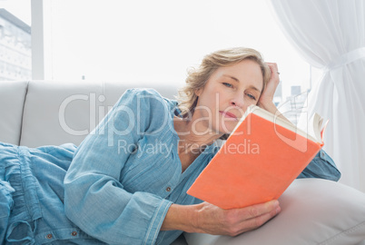 Content blonde woman relaxing on her couch reading book