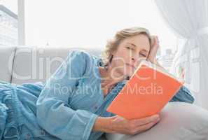 Content blonde woman relaxing on her couch reading book