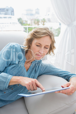 Content blonde woman relaxing on her couch using her tablet
