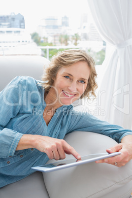 Happy blonde woman relaxing on her couch using her tablet Happy blonde woman relaxing on her couch using her tablet