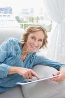 Happy blonde woman relaxing on her couch using her tablet