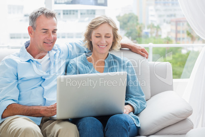 Cheerful couple relaxing on their couch using the laptop