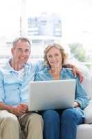 Smiling couple relaxing on their couch using the laptop