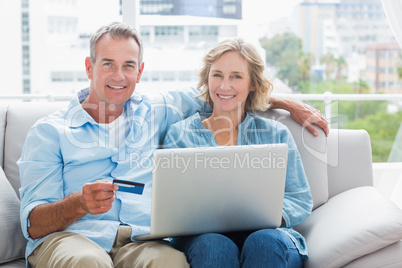 Happy couple sitting on their couch using the laptop to buy onli