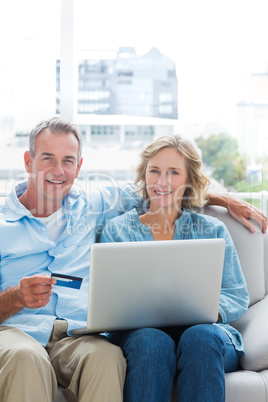 Cheerful couple sitting on their couch using the laptop to buy o