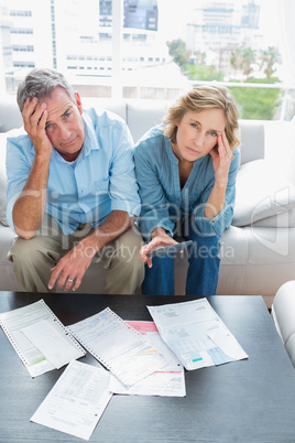 Anxious couple sitting on their couch paying their bills
