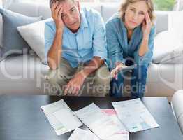 Stressed couple sitting on their couch paying their bills