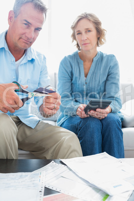 Husband cutting credit card in half with wife with bills on the