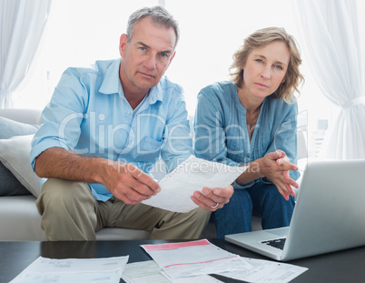 Worried couple paying their bills online with laptop looking at