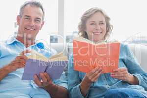 Relaxed couple reading books on the couch smiling at camera