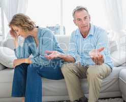 Arguing middle aged couple sitting on the couch with man gesturi