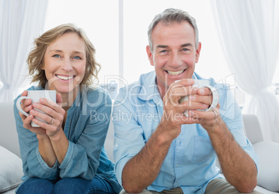 Smiling middle aged couple sitting on the couch having coffee