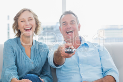 Laughing middle aged couple sitting on the couch watching tv