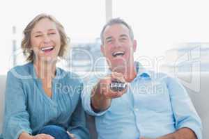 Laughing middle aged couple sitting on the couch watching tv